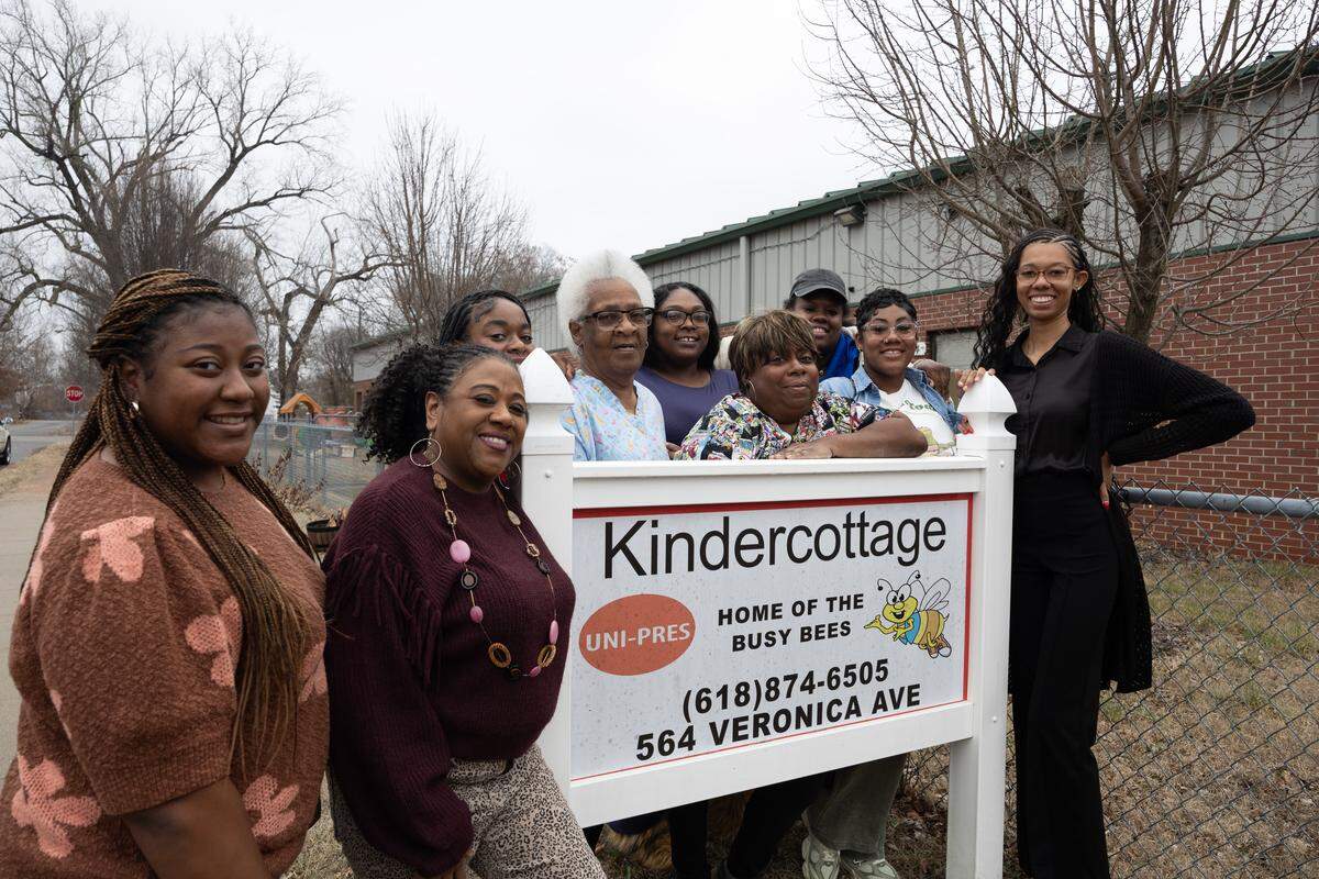 The staff at UNI-Pres Kindercottage in East St. Louis pose outside the sign leading to their building. “We’ve always been advocates for whatever benefits the children,” said Aimee Hart, the center’s director.