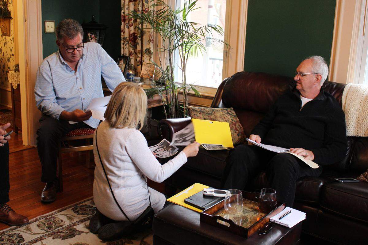 Doug Wombacher, left, his wife, Ruth, and his friend, Eddie Morrison, look at old photos and newspaper clippings related to the 1969 murder of Eddie’s brother, Mike.