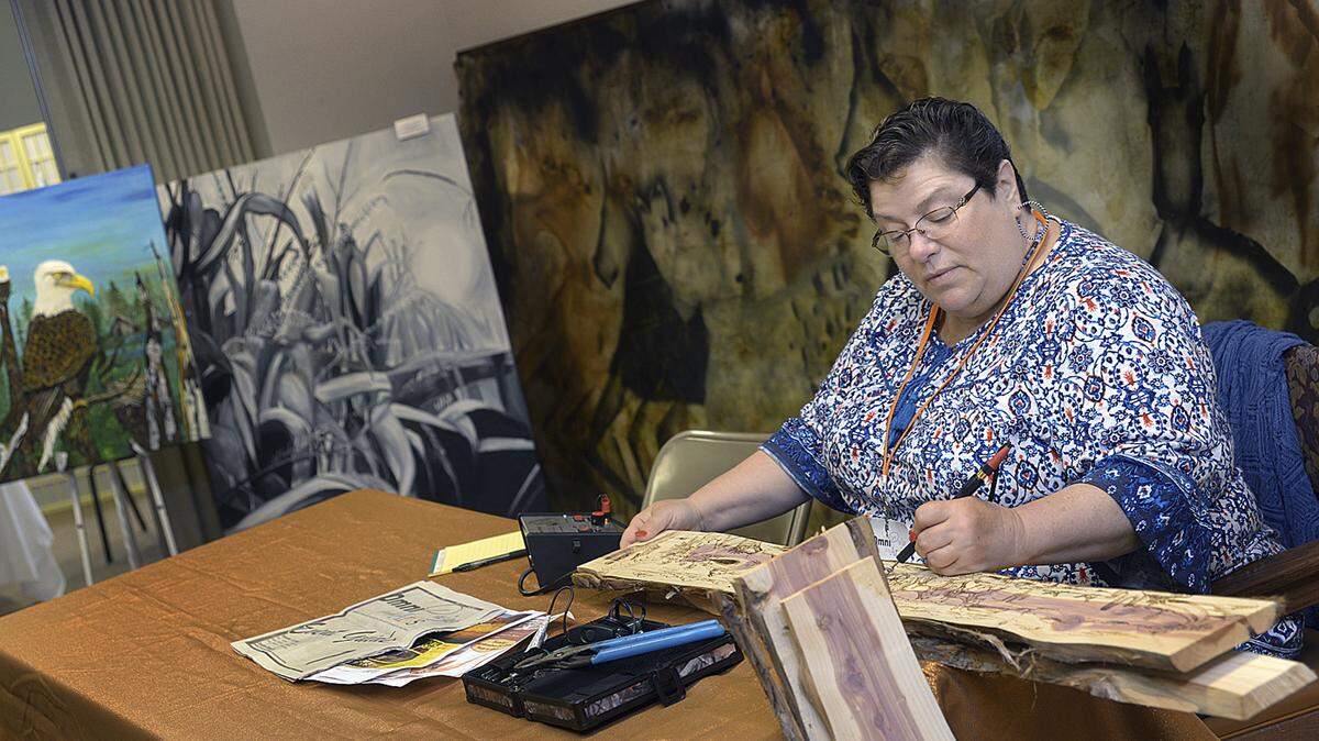 In this Sept. 7,  photo Mary “Kathy” Zehr woodburns a piece in front of visitors at the Reddick Mansion for the Omni Prize for the Arts festival in Ottawa, Ill. Zehr entered the piece sitting behind her into the competition which was made with a process involving smoke bombs and gunpowder.