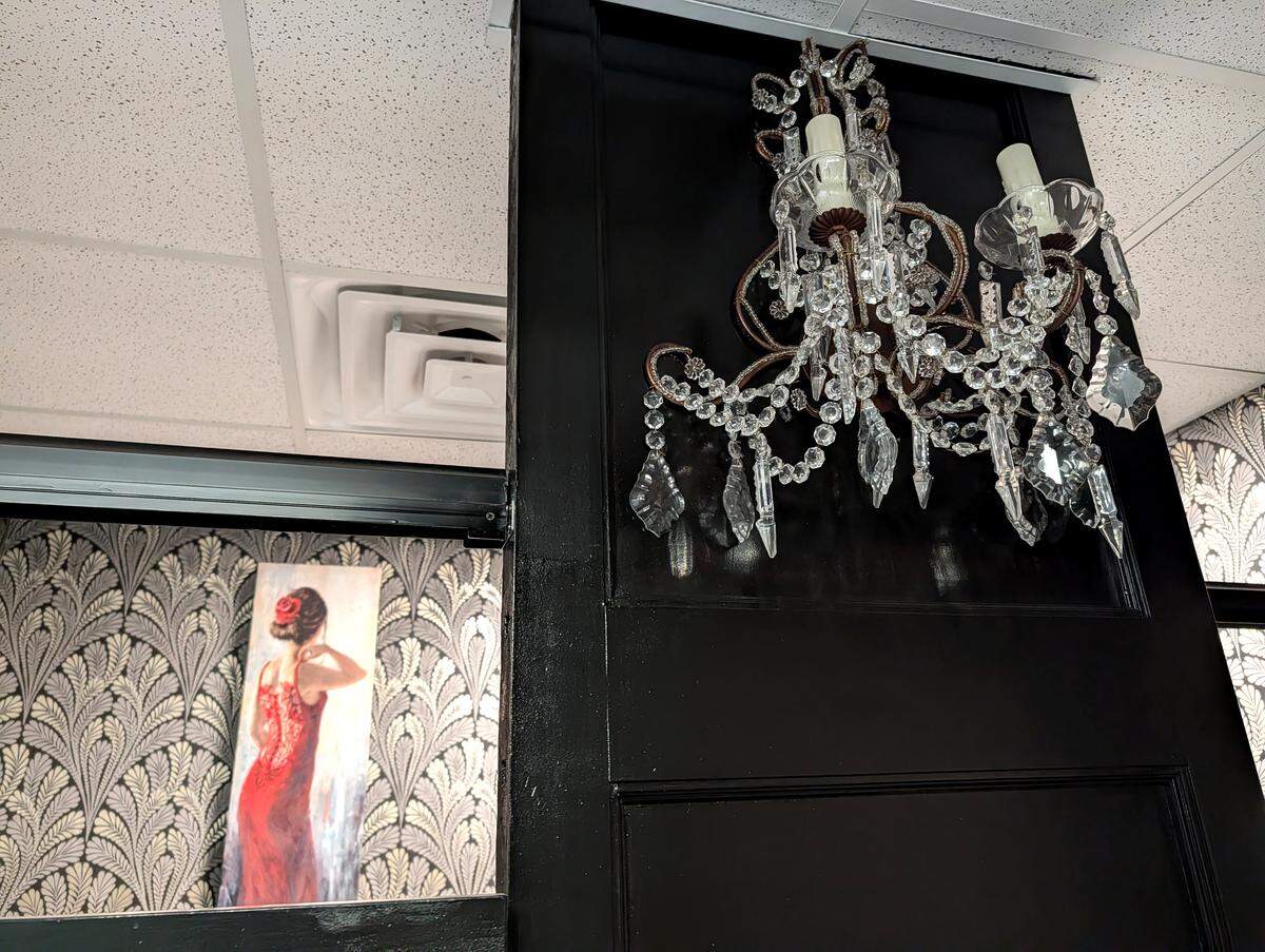 Details in the ladies' restroom include a chandelier wall sconce, ornately detailed wallpaper and art.