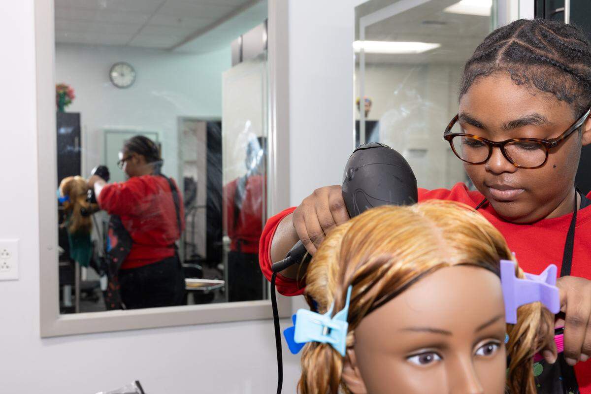A student in a cosmetology class at East St. Louis Senior High School practices hair drying techniques on a mannequin head.