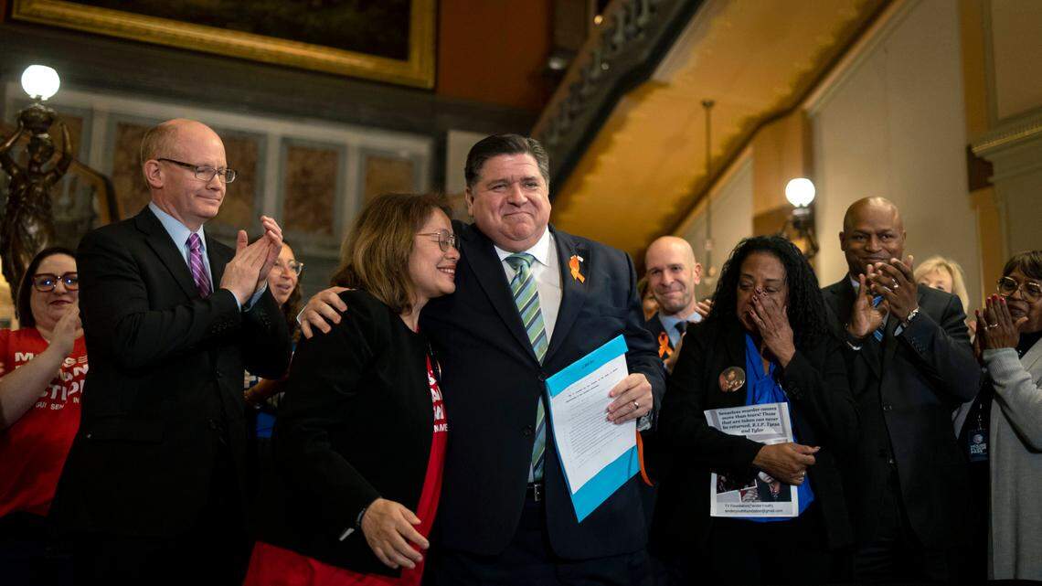 Gov. J.B. Pritzker hugs gun control advocate Maria Pike after he signed comprehensive legislation to ban military-style firearms on Tuesday, Jan. 10, 2023, at the Illinois State Capitol in Springfield, Ill. Pike lost her son, Ricky, to gun violence. Advocate Delphine Cherry, third from right, who lost her children Tyesa and Tyler to gun violence, wipes away tears.