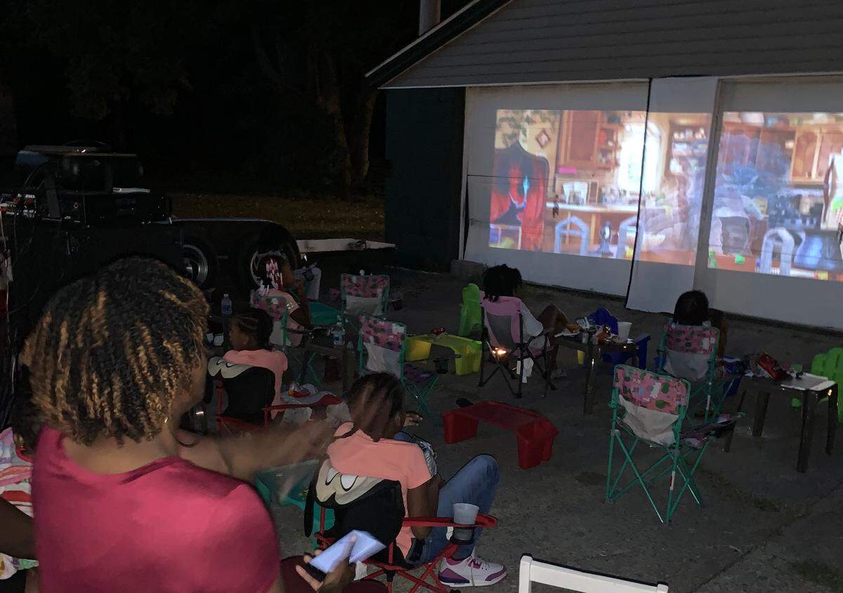 Families watch a movie together during the first movie night. Zoe Howlett, 6, her mother Tieara Moore and their family are working together to have a lemonade stand and movie night in their community.