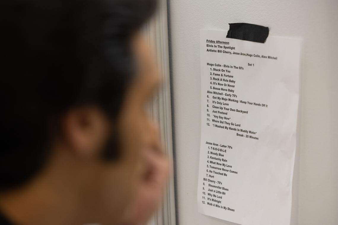 An Elvis tribute actor puts on makeup while a setlist for other Elvises is posted in the background.