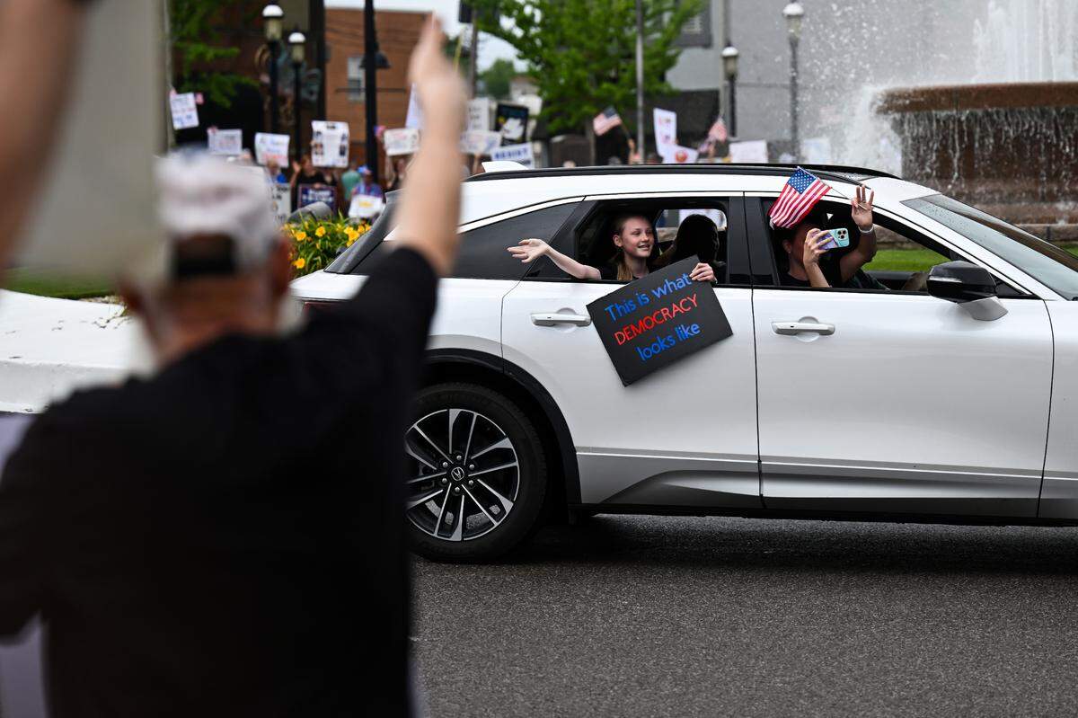 A passenger in a passing car waves to protesters at the “No Kings” demonstration in Belleville’s Public Square Saturday, June 14, 2025.