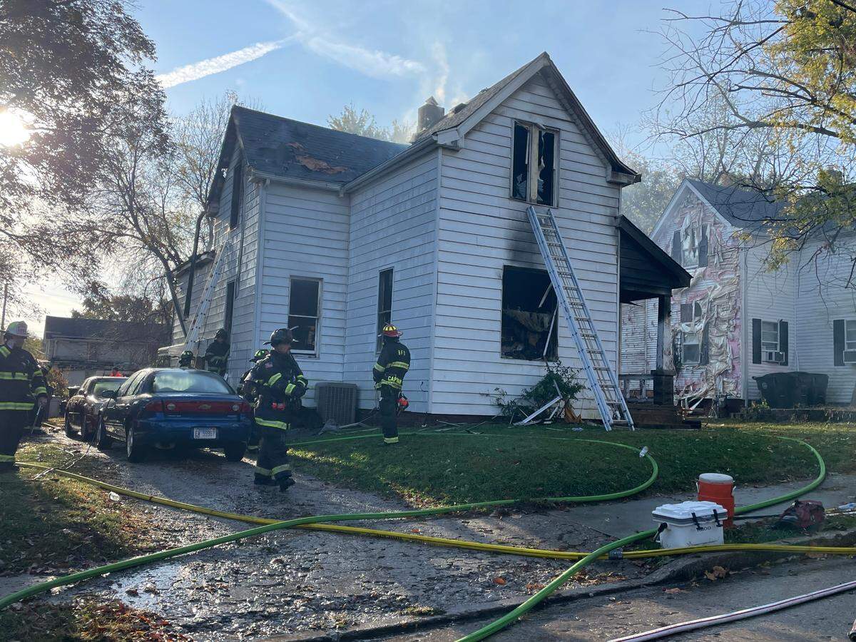 Firefighters work the scene of a fatal house fire in the 100 block of South 13th Street. Melted siding on the neighboring home can be seen.