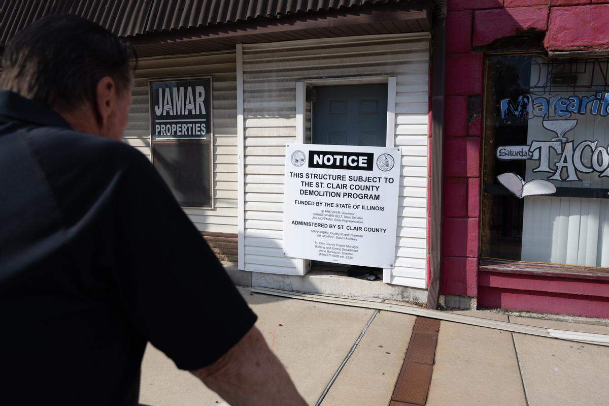 Belleville Historic Society President Larry Betz reads a sign on Monday that identifies a storefront at 1013 W. Main St. as a “structure subject to the St. Clair County Demolition Program.”