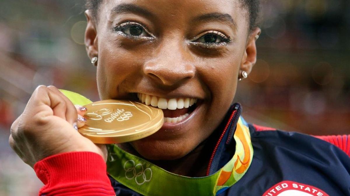 United States' Simone Biles bites her gold medal for the artistic gymnastics women's individual all-around final at the 2016 Summer Olympics in Rio de Janeiro, Brazil, Thursday, Aug. 11, 2016.