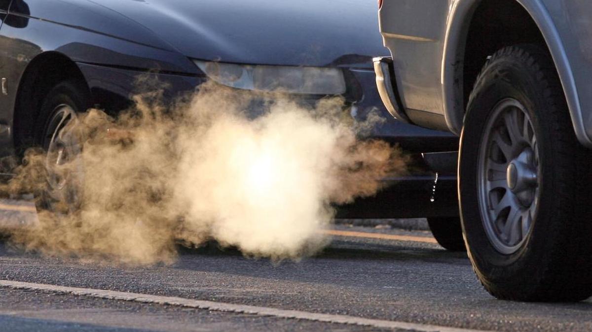 A cloud of smoke and water vapor blows from muffler of a pickup truck stopped at a traffic light.