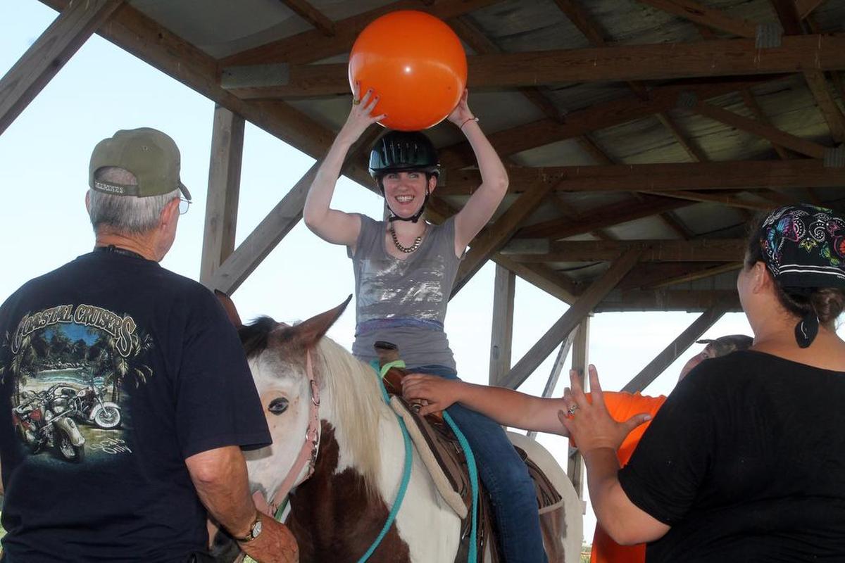 Molly Carver, 25, of Edwardsville, gets ready to toss a ball during a horsemanship therapy session at Chakota Therapeutic Riding Center. The exercise helps her with flexibility, balance and range of motion.