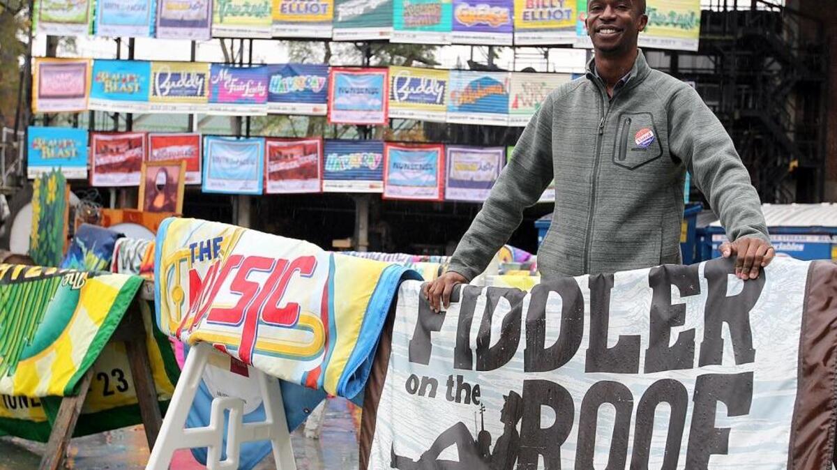 Kwofe Coleman, director of marketing and communications at The Muny, displays some of the large show banners that will be sold Saturday at the garage sale. They’re priced at $20 to $35 each.