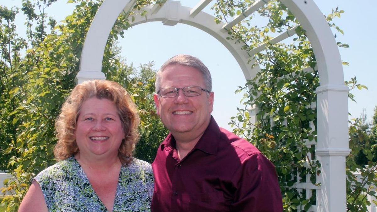Arla and David Chevess stand in front of an 8-foot arch that leads into a backyard full of fruit trees, bushes, plants and a vegetable garden. Yellow roses are now in bloom.