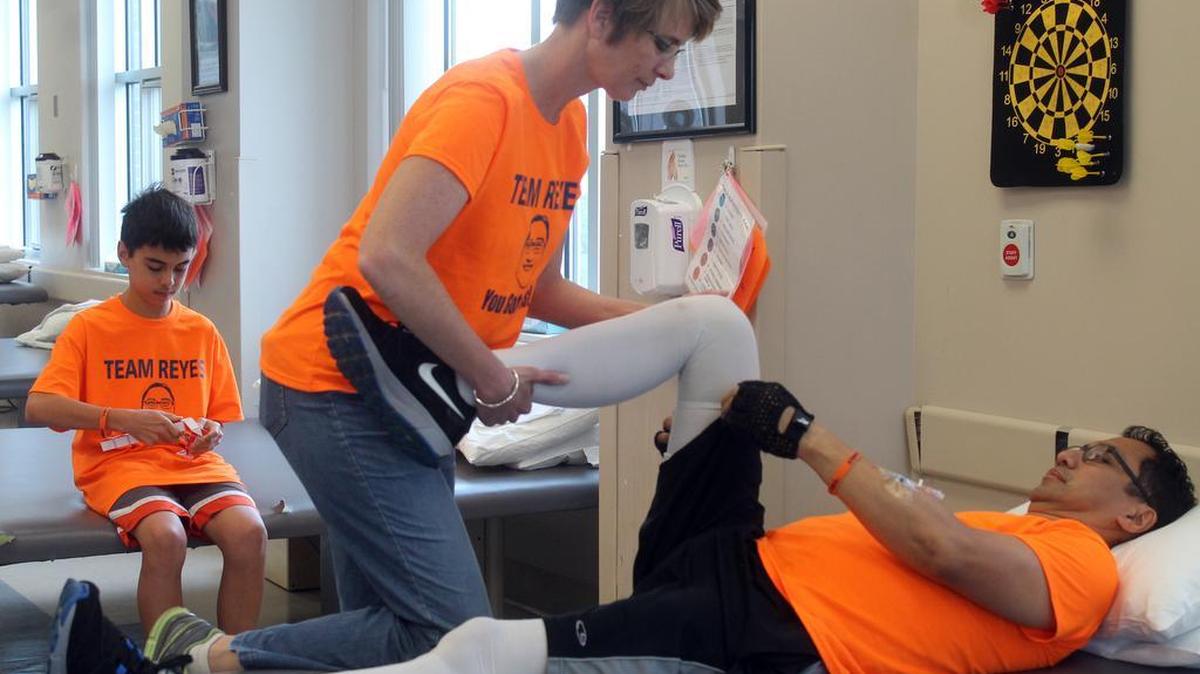 Karen Reyes helps her husband Eric with stretching exercises to help maintain muscle tone. Because of a 12- to 15-foot fall from a tree on March 26, Eric is paralyzed from the waist down. Son Zachary, 12, sits behind them.