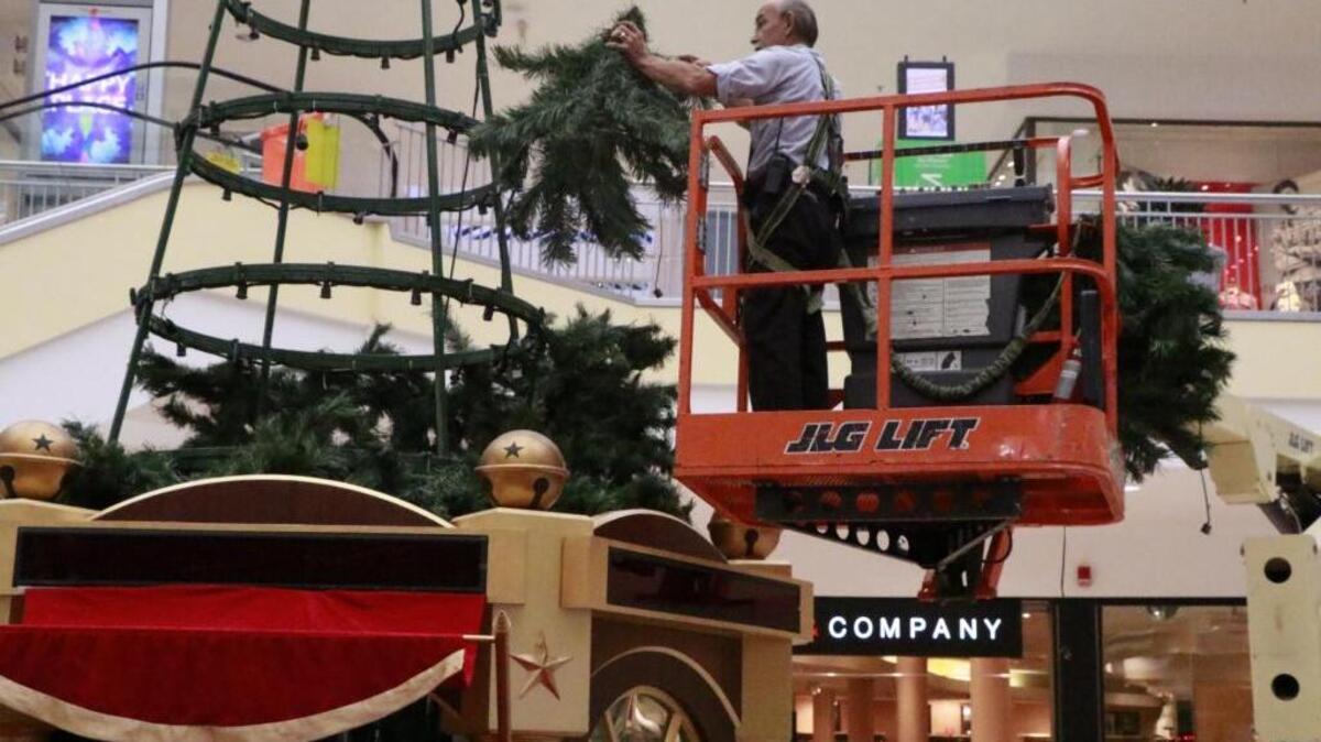St. Clair Square maintenance technician Victor White uses a boom lift to hook greenery sprays on the steel frame of a 35-foot-tall Christmas tree in Center Court on Thursday.