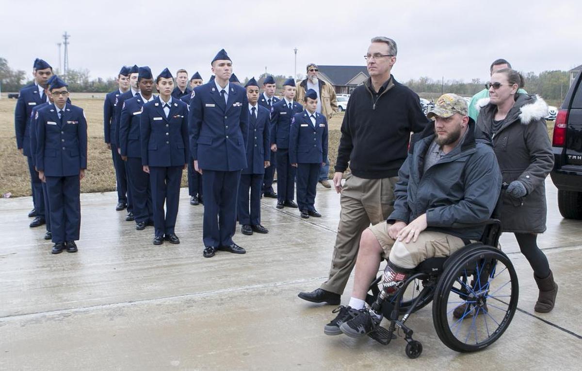Operation Finally Home executive director Rusty Carroll escorts U.S. Marine Lance Corporal James Poggi and his wife Stefanie to the location of their future home in the Brickyard Lake estates in Mascoutah. Members of the Mascoutah Air Force JROTC stand at attention at the start of the groudbreaking ceremony.