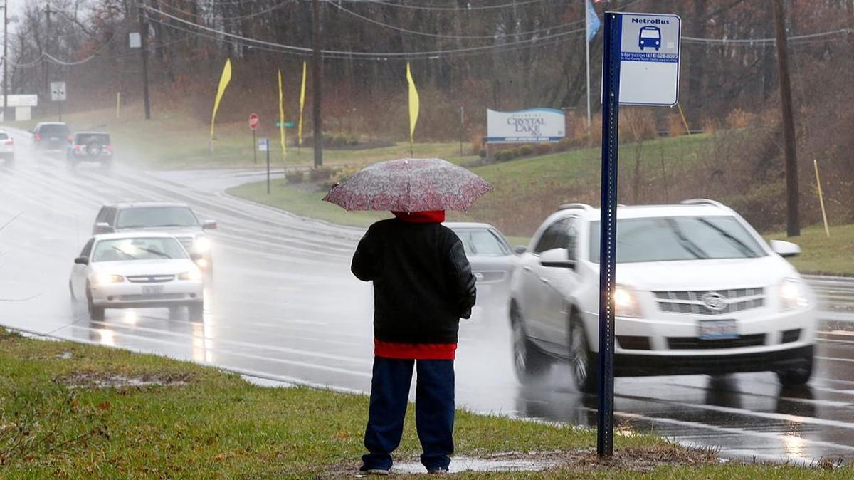 A pedestrian waits in the rain for a bus Sunday as traffic passes on Illinois 159 in Fairview Heights.