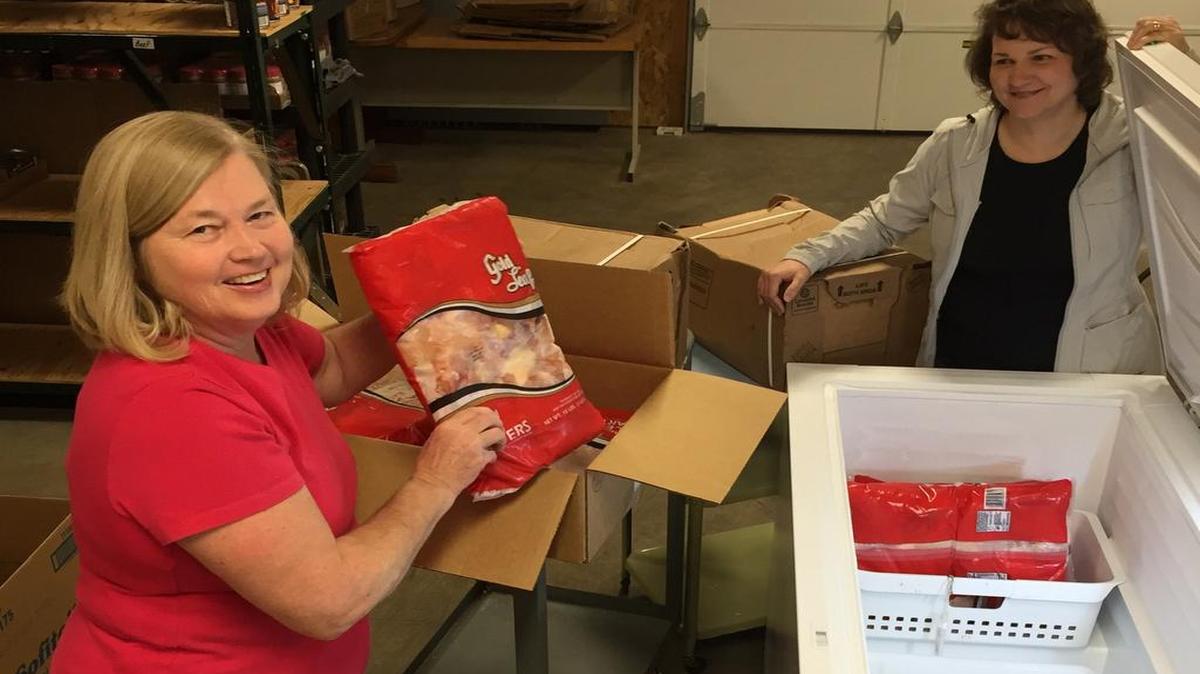 Teresa Boudouris, new associate director of the Highland food pantry, loads USDA frozen chickens into HACSM’s new freezer, which was purchased with money from the Highland Area Community Foundation grant. Diane Williams looks on in the background on the right.
