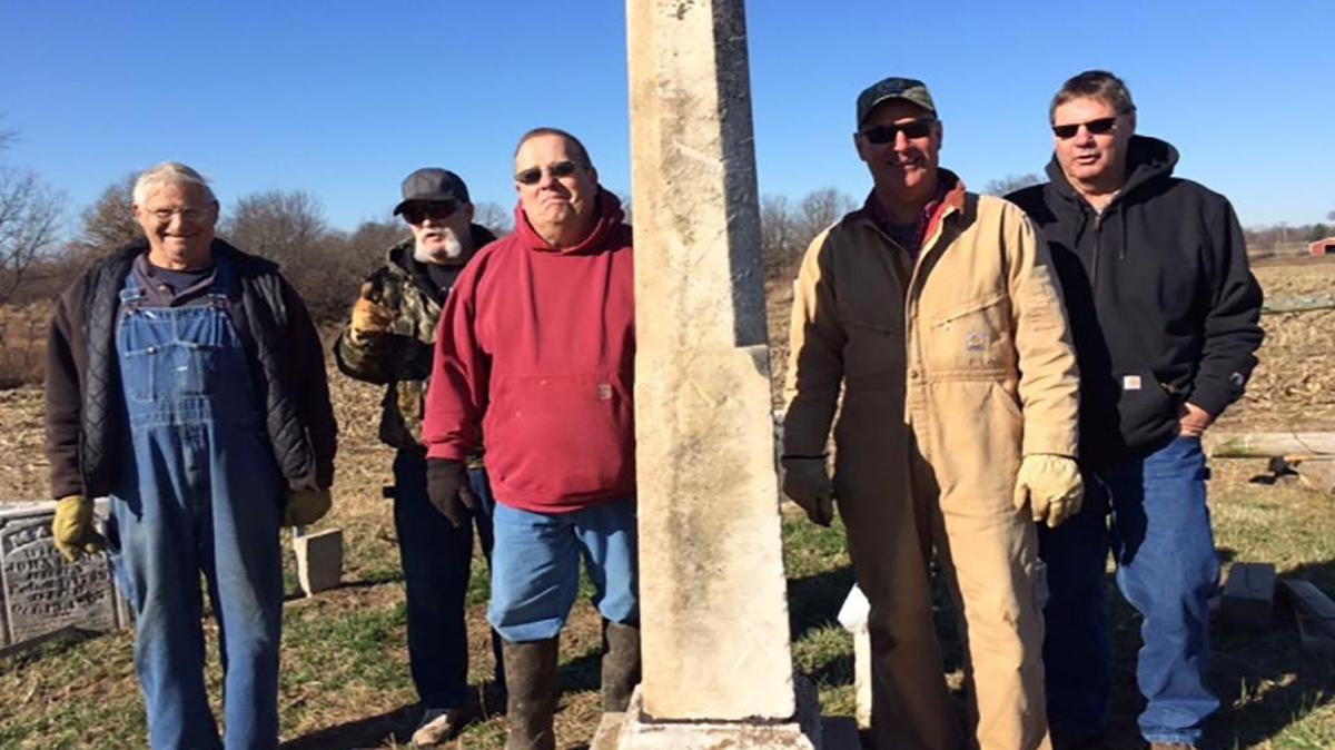 A group of volunteers stands near Maj. James G. Anderson’s obelisk tombstone.
