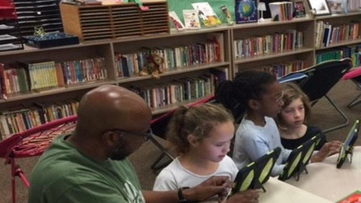 Goerge Mitchom assists fifth-grade students Sarah Huller, Alana Mitchom and Mariah Huller during “Hour of Code” at LaVerna Evans Elementary in O’Fallon with the school tablets.