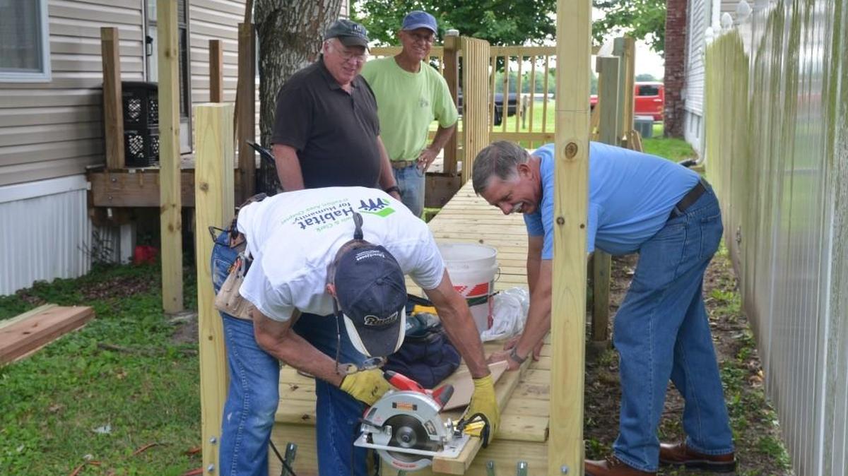 From left back, O’Fallon Habitat For Humanity President Ken Beeman and Roy Carlson, both Thrivant Financial’s Thrivant Builds/Repairs members look on while Leonard Wojtysiak, of Faith Lutheran Church, works the saw, and Jim Campbell, of Faith Lutheran and the O’Fallon Rotary Club, braces the 2-foot by 4-foot beam for the wheelchair ramp guardrail.