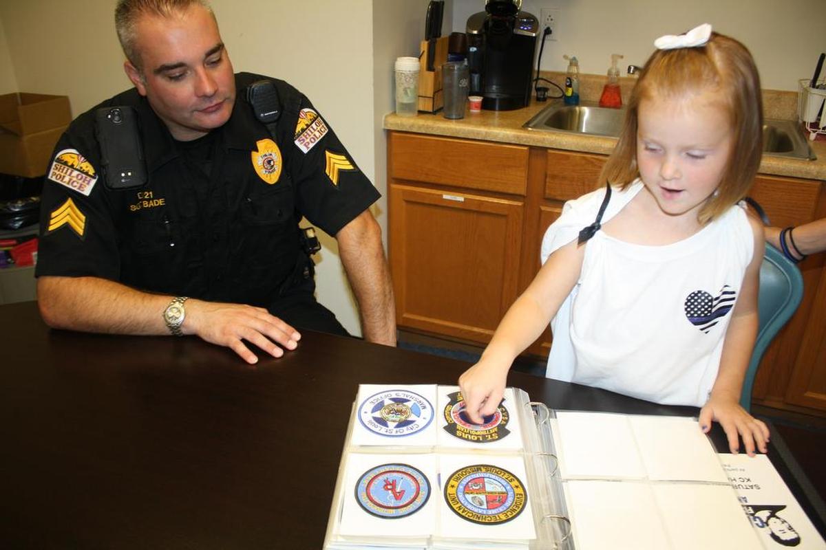 Tinley Kern, 5-year-old Shiloh youth shows Shiloh Police Sgt. Kyle Bade her growing collection of, now 98, police department patches that departments from all over the United States have sent her, including one she received from Queensland Police in Australia.