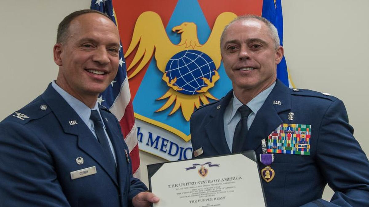 Col. Douglas Curry, 375th Medical Group commander, presents Lt. Col. Steven Fisher with the Purple Heart during a ceremony Aug. 12 at Scott Air Force Base. On Oct. 17, 2011, Fisher was injured in the line of duty during a rocket attack while deployed to Afghanistan.