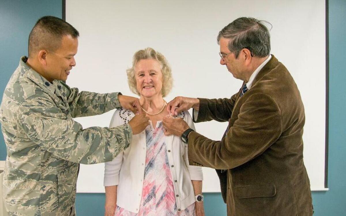 Karen Bunch, Cyberspace Support Squadron mission readiness training manager, receives commemorative pins from Lt. Col. Eric Trias, Cyberspace Support Squadron commander, and her husband Kenneth to celebrate 50 years of dedicated service to the Air Force during a Wingman Day luncheon at Scott.