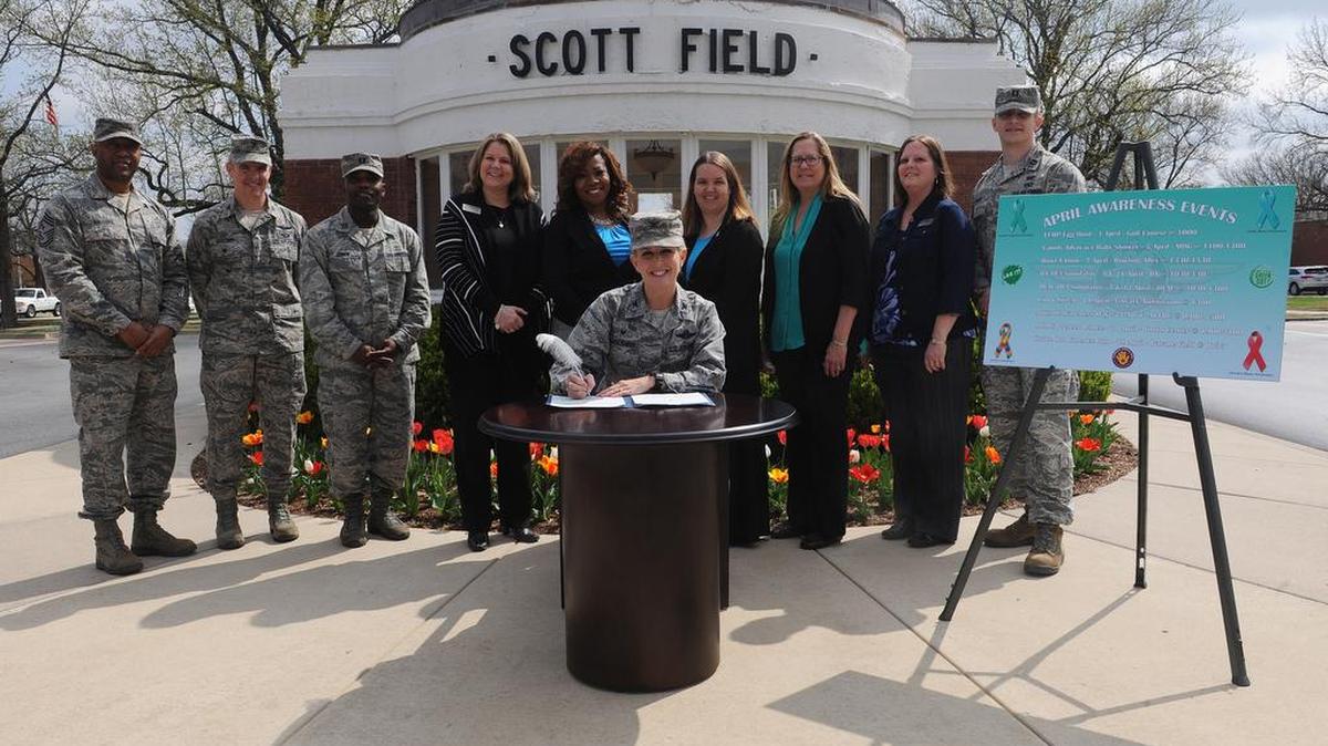 Col. Laura Lenderman, 375th Air Mobility Wing commander, signs an awareness proclamation April 4 in front of the historical gate. This year, the base is combining Sexual Assault Awareness Month, Green Dot, Alcohol and Drug Prevention and Treatment, Child Abuse Prevention, Autism Awareness, and Month of the Military Child under one unified effort to raise awareness about those campaigns. Back row: Chief Master Sgt. Wesley Mathias, 375th AMW command chief; Col. William Buschur, 375th AMW vice commander; Capt. Ed Jones, Alcohol and Drug Prevention and Treatment program manager; Shannon Dauber; Airman and Family Readiness airman and family services chief; Mauranda Bembry, 375th Medical Group Family Advocacy program manager; Jamie Mattice, 375th AMW Sexual Assault Program and Response specialist; Brenda Wells, 375th AMW primary prevention of violence specialist; Monica Stouffer, A&FRC chief; and Capt. Travis Hough, SAPR deputy sexual assault response coordinator.