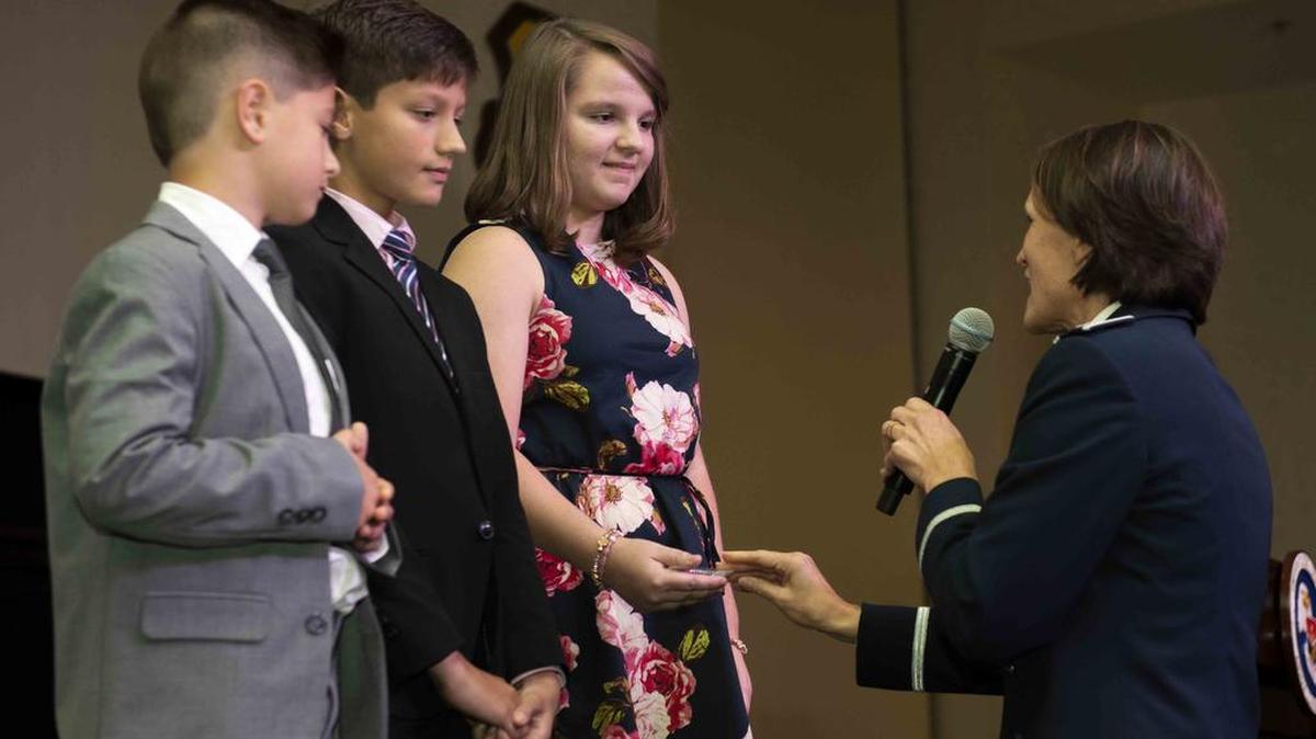 Eliana, Tristan and Caleb, children of fallen Master Sgt. Gregory Kuhse from the 3rd Manpower Requirements Squadron, receive coins from Col. Leslie Maher, 357th Air Mobility Wing commander, at the Class 18-G Airman Leadership School graduation, Oct. 11, 2018. This moment was part of the school’s new legacy project meant to honor past service members. Kuhse and Maj. Phyllis Pelky were killed in a 2015 helicopter crash in Afghanistan.