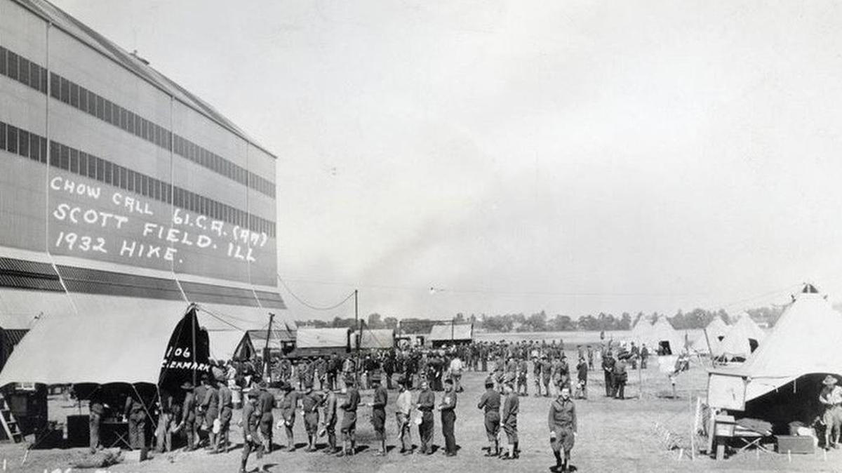 SCOTT THROUGH THE YEARS: Scott Field members take a break for chow during a 1932 hike alongside the massive airship hangar, which housed large airships and observation balloons until the late 1930s. This structure was easily noticeable for miles around, and was the second largest airship hangar in the world at the time.