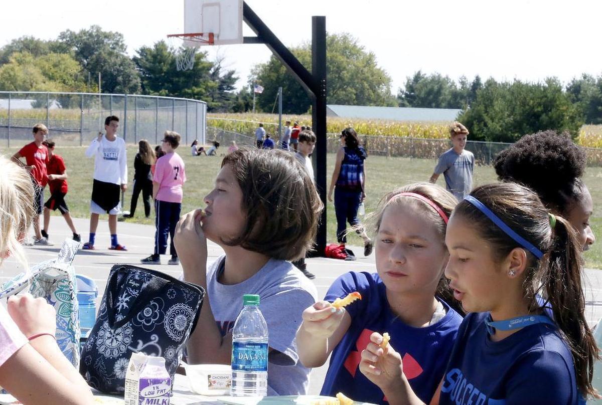 Wolf Branch Middle School 7th-graders Lauren Pugeda (from left), Emily Messinger and Olivia Pereda eat lunch on picnic tables on the school's playground while other students play basketball in the background. Students will either eat in the halls or on the playground now that the cafeteria seating area is closed off.