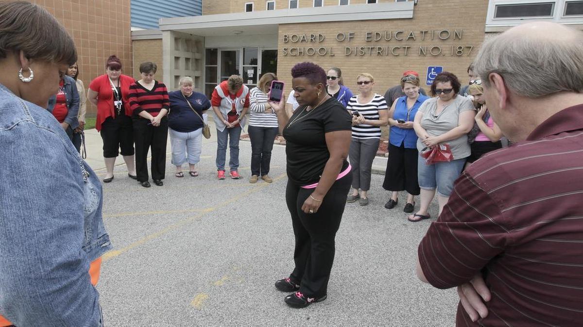 
About 50 people gathered Friday afternoon outside the Cahokia school board office to honor longtime teacher Mary Hartrum, who died of cancer, with a balloon release. Before they released the 50 pink balloons, they observed a moment of silence, played a song that characterized Hartrum's life, and gave out gifts to her many grandchildren, whom she loved dearly. Here, people bow their heads during a moment of silence and as Patrice Harris (center) - who organized the event and taught for many years with Hartrum - holds up a phone as it plays the song in memory of Hartrum. 
