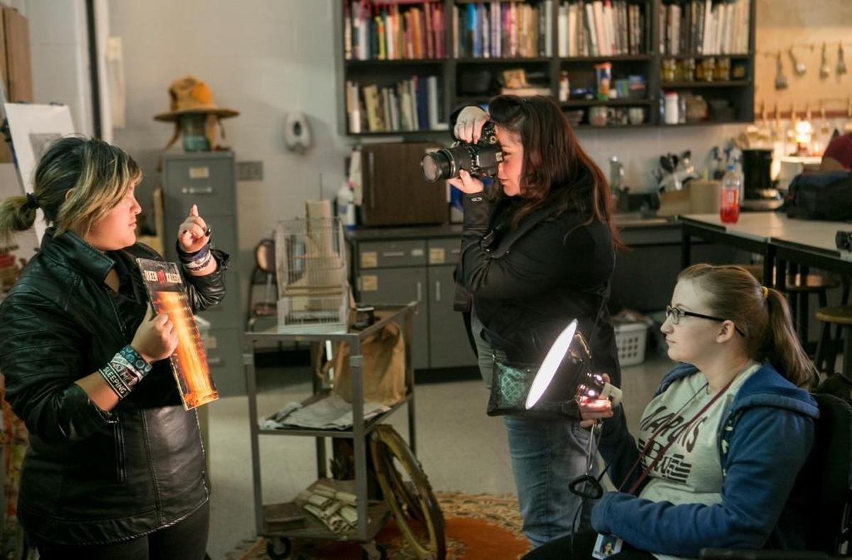 Belleville West High School senior Yolanda Cartagena prepares to get her portrait taken by art teacher Cari Casper-Bassler. Senior Emily Schnarr helps hold the light for the portrait.
