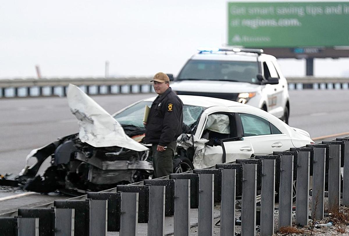 An Illinois State Police officer stands by one of the wrecked vehicles Sunday on the west-bound side of I-64 near Washington Park.