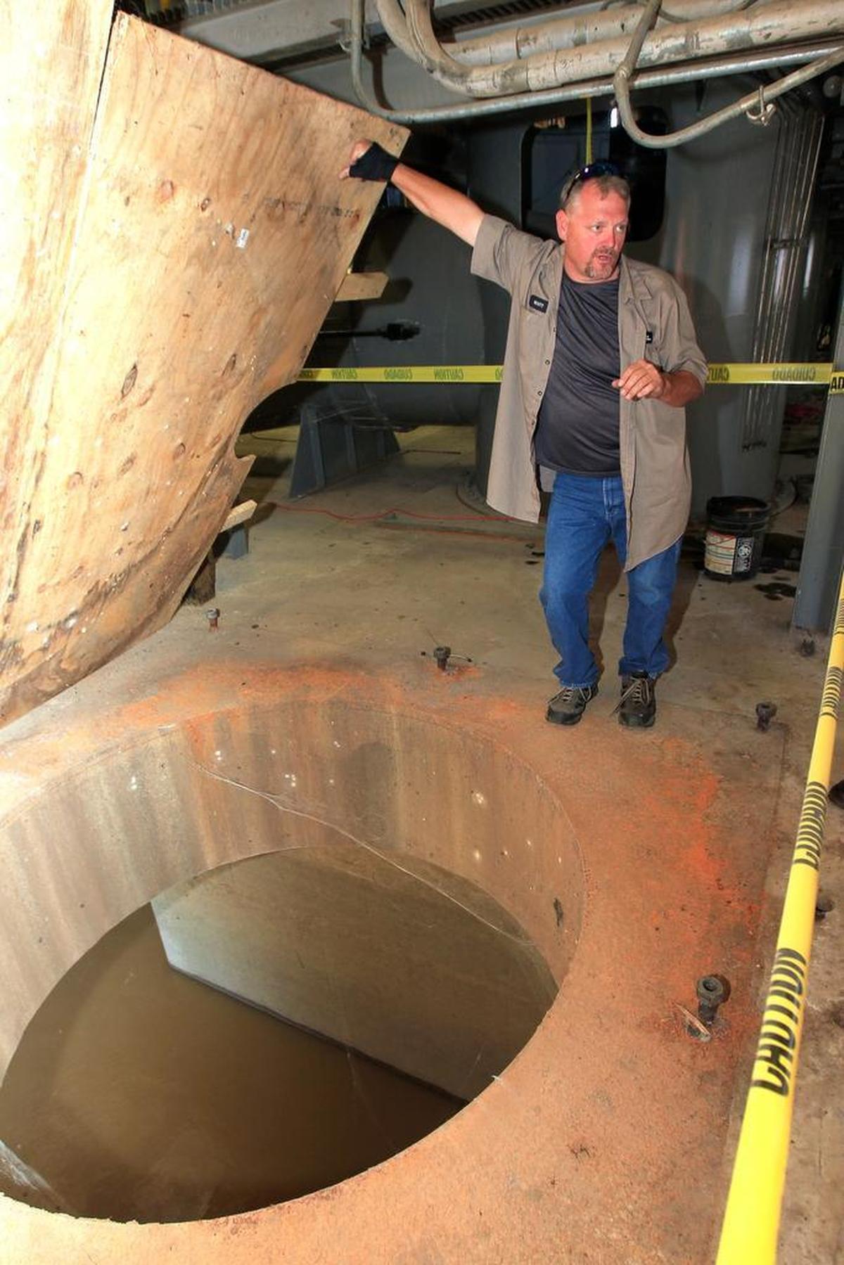 Scott Hillman, a pump operator with the Metro East Sanitary District, holds open a plywood safety cover over a hole in the floor of the East St. Louis riverfront pumping station. An enormous pump normally sits inside a huge metal tube in the hole and rests underwater here, where the Cahokia Canal flows into the Mississippi River. The pump has been removed for servicing.