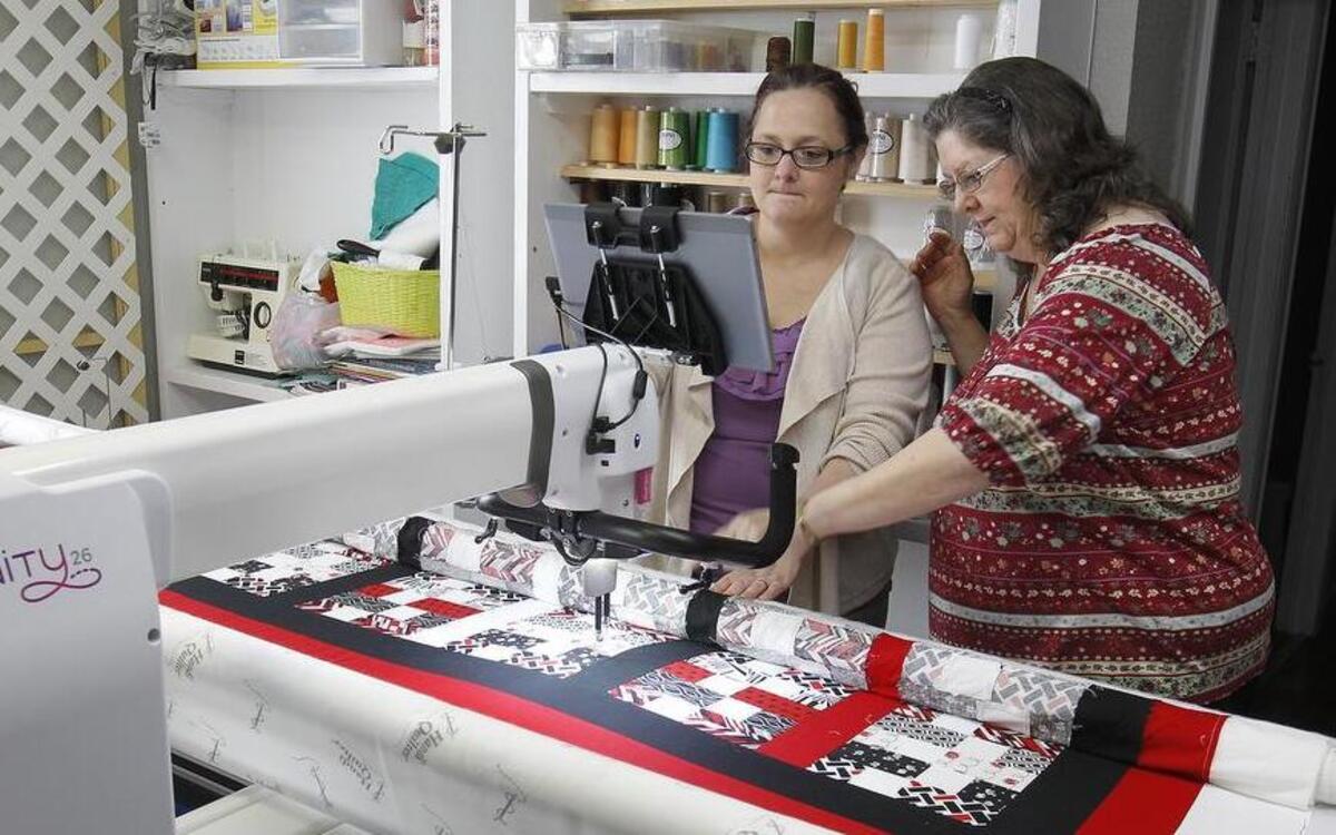 Danielle Cyvas (left) and her mother Debbie Chitty operate the Warm N Cozy Quilting business at 235 North Main Street in Columbia. Here they are inputting a program into their computerized longarm industrial sewing machine to sew a pattern onto a customer's quilt.