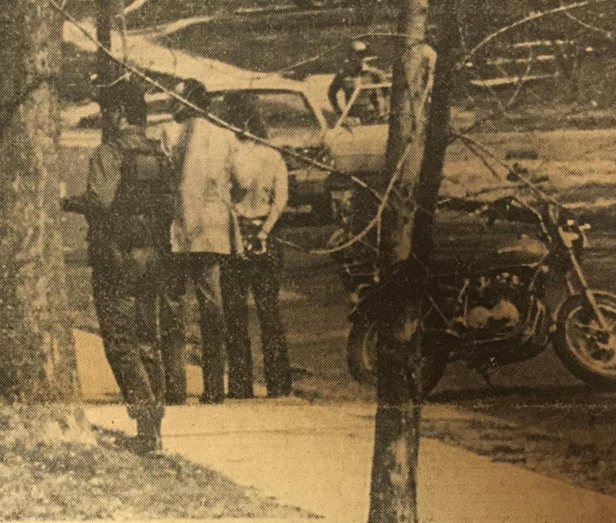 John Scott ‘Li’l Wolf’ Killip, shirtless and handcuffed, stands on sidewalk.