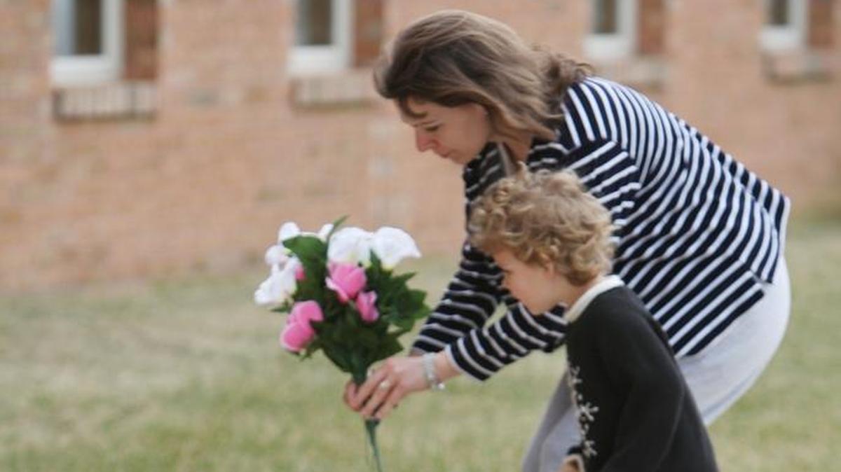 Emma Lozowski and her daughter Ingrid leave some flowers on the memorial left for Rev. Fred Winters outside the First Baptist Church in Maryville.