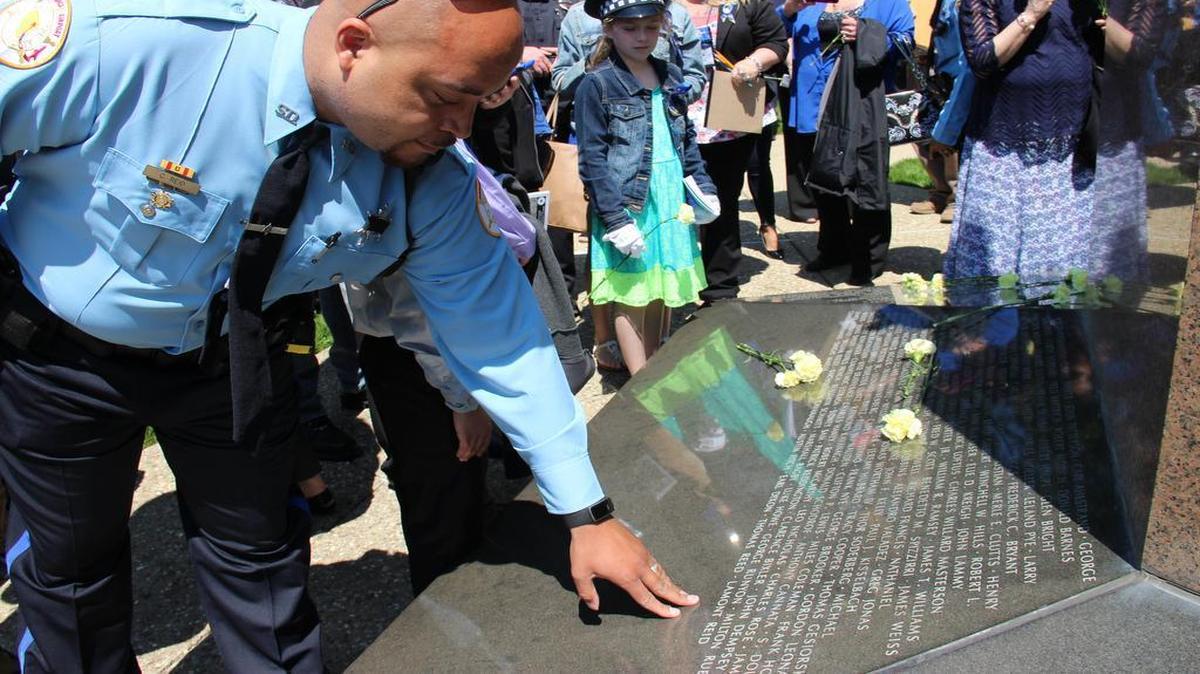 St. Clair County Sheriff’s Corrections Officer Cameron Reid places his hand by his father’s name on the memorial. Lamont Reid also worked for the sheriff’s department and died on duty in 2010 from a heart attack.