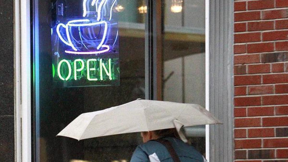 A pedestrian walks in the rain as she passes a sign for hot coffee at Junction Coffee and Yogurt Bar in downtown Belleville. Junction Coffee & Frozen Yogurt closed Sunday after five years of business.