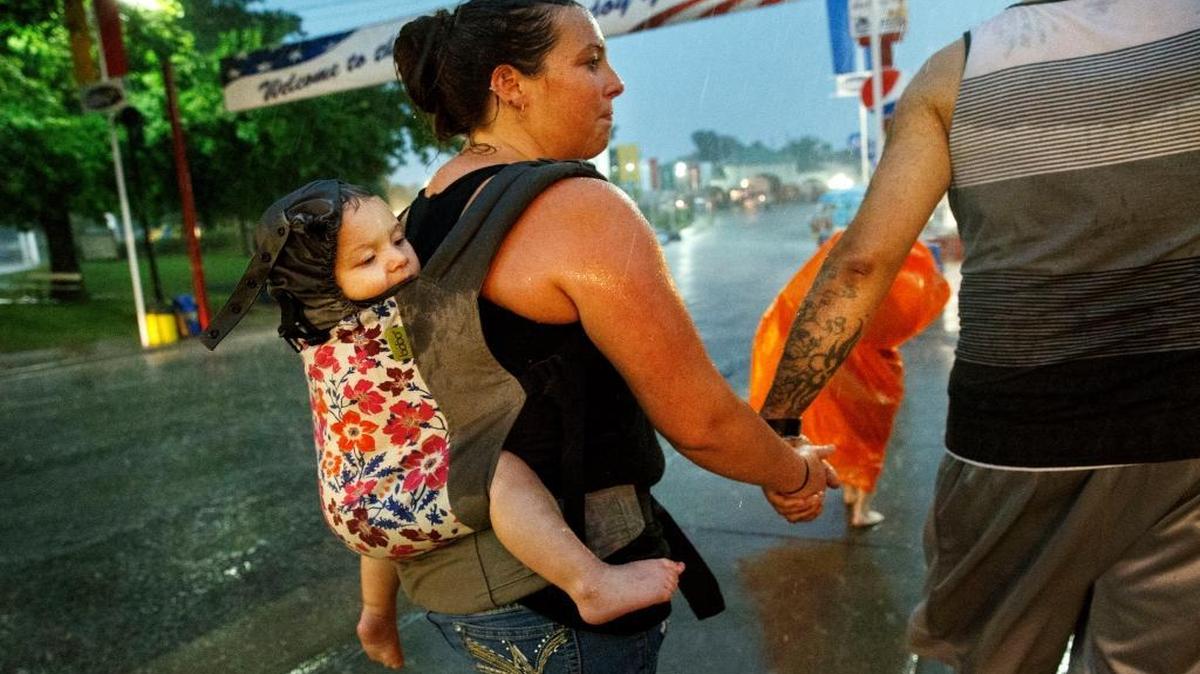 In this Friday, Aug. 12, 2016 file photo, Christi Gaskin carries her daughter Alexia Belcher on her back as she makes her way back to the car with husband Bradley Belcher and her son Dayne during a downpour at the Illinois State Fairgrounds in Springfield. The torrential rains flooded streets on the fairgrounds and surrounding areas.