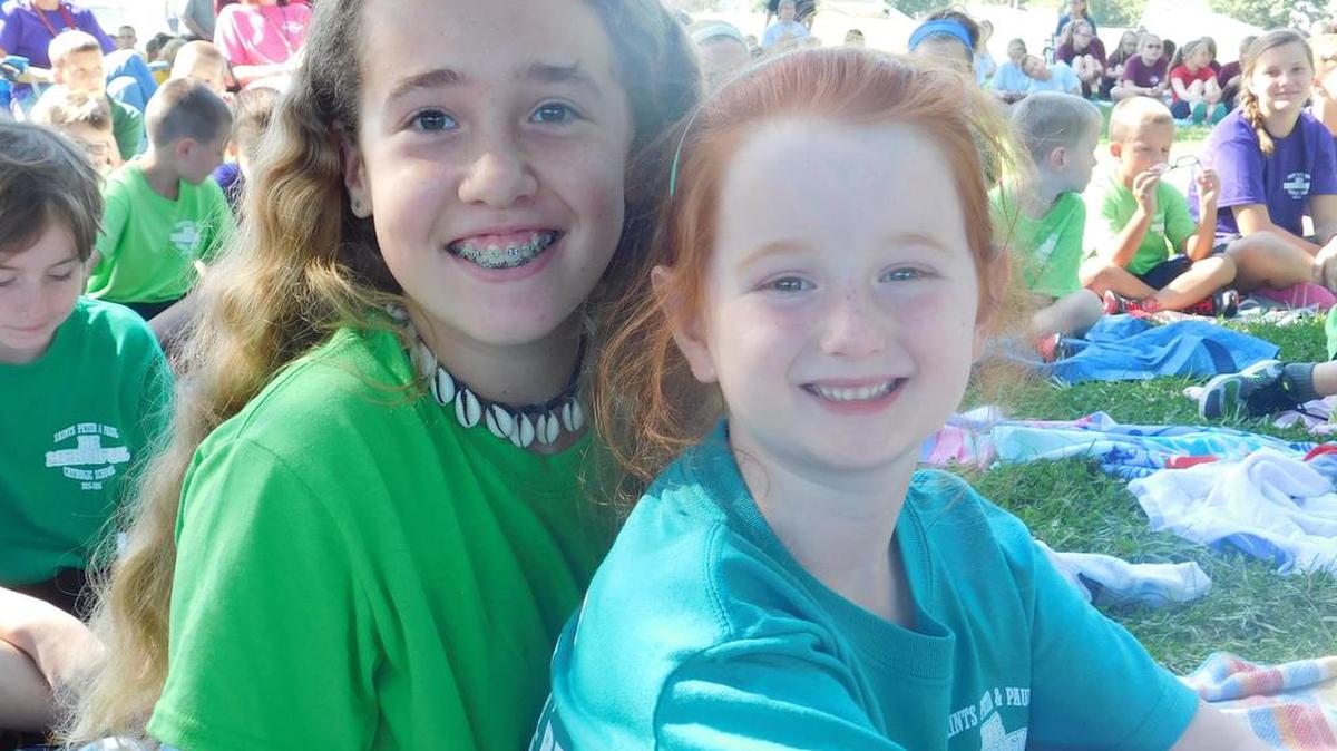 
Kindergartener Audrey Essner sits with her eighth grade buddy, Hannah Gundlach, while they wait for outdoor Mass at the Saints Peter and Paul Church School fields in Waterloo.
