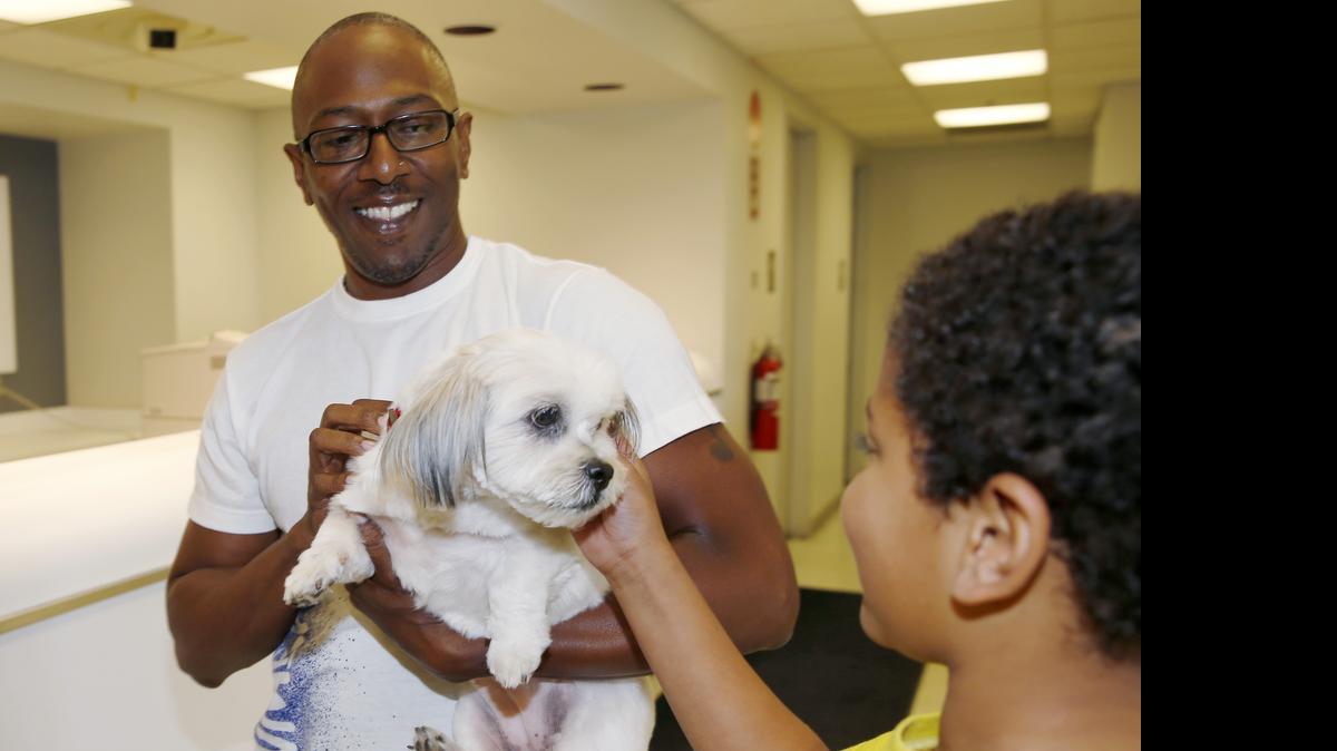 
Kelly Booker shows his son, Azzah, their long lost dog, Lilly the Shih Tzu, at the United Airlines cargo terminal Thursday in Denver. Lilly, who disappeared nearly four years ago from her owner’s home in west Denver on July 4, 2011, was found wandering the streets of the Chicago suburb of Elgin and nursed back to health. She was identified by a microchip with her owner’s contact information.
