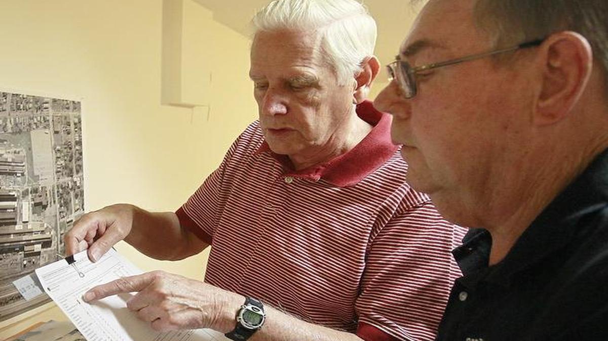 Retired Dow Chemical Co. workers Bill Hoppe, center, and Don Thompson look over lists of radioactive elements that were checked while they worked there. Both say they suffered cancers as a result of exposure to radioactive elements such as cadmium, uranium, beryllium, and lithium while on the job. The map on the wall shows an aerial view of the Dow Chemical plant and the boxes on the table are full of records Hoppe has gathered over the years.
